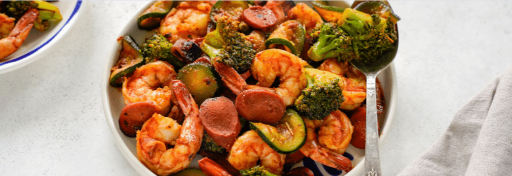 A white bowl of cajun shrimp and sausage with vegetables