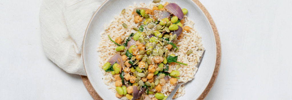 A white bowl filled with a sauteed chickpea and edamame recipe with rice and vegetables