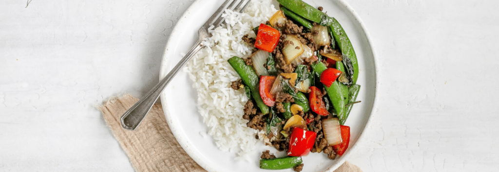A white plate with jasmine rice, and thai basil beef stir fry
