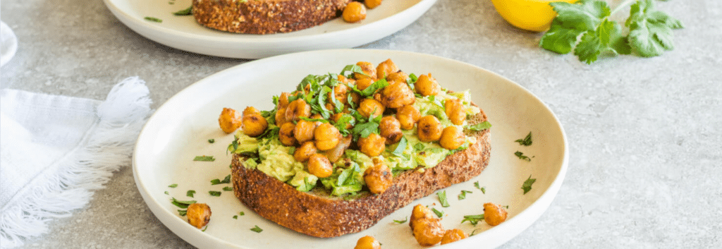 A white plate with an open-faced toast with avocado and chickpeas