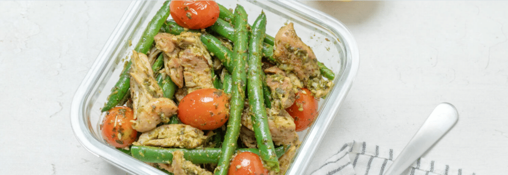 A pyrex container filled with pesto chicken, green beans and cherry tomatoes