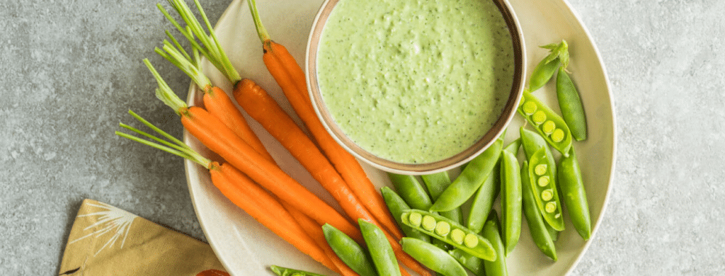 A plate of spring pea and feta dip with carrots and peas