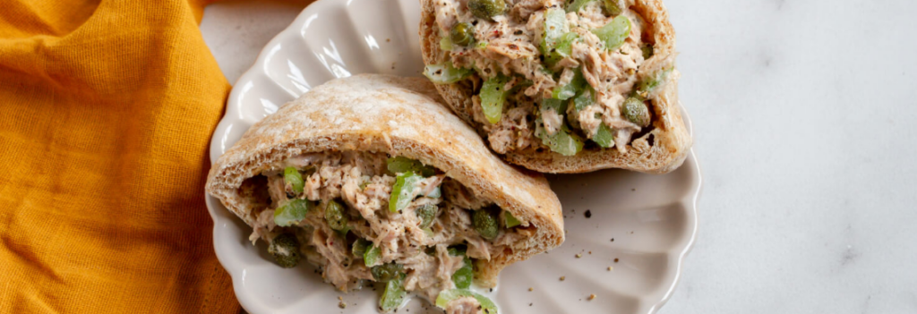 A white plate of tuna stuffed pita with an orange napkin